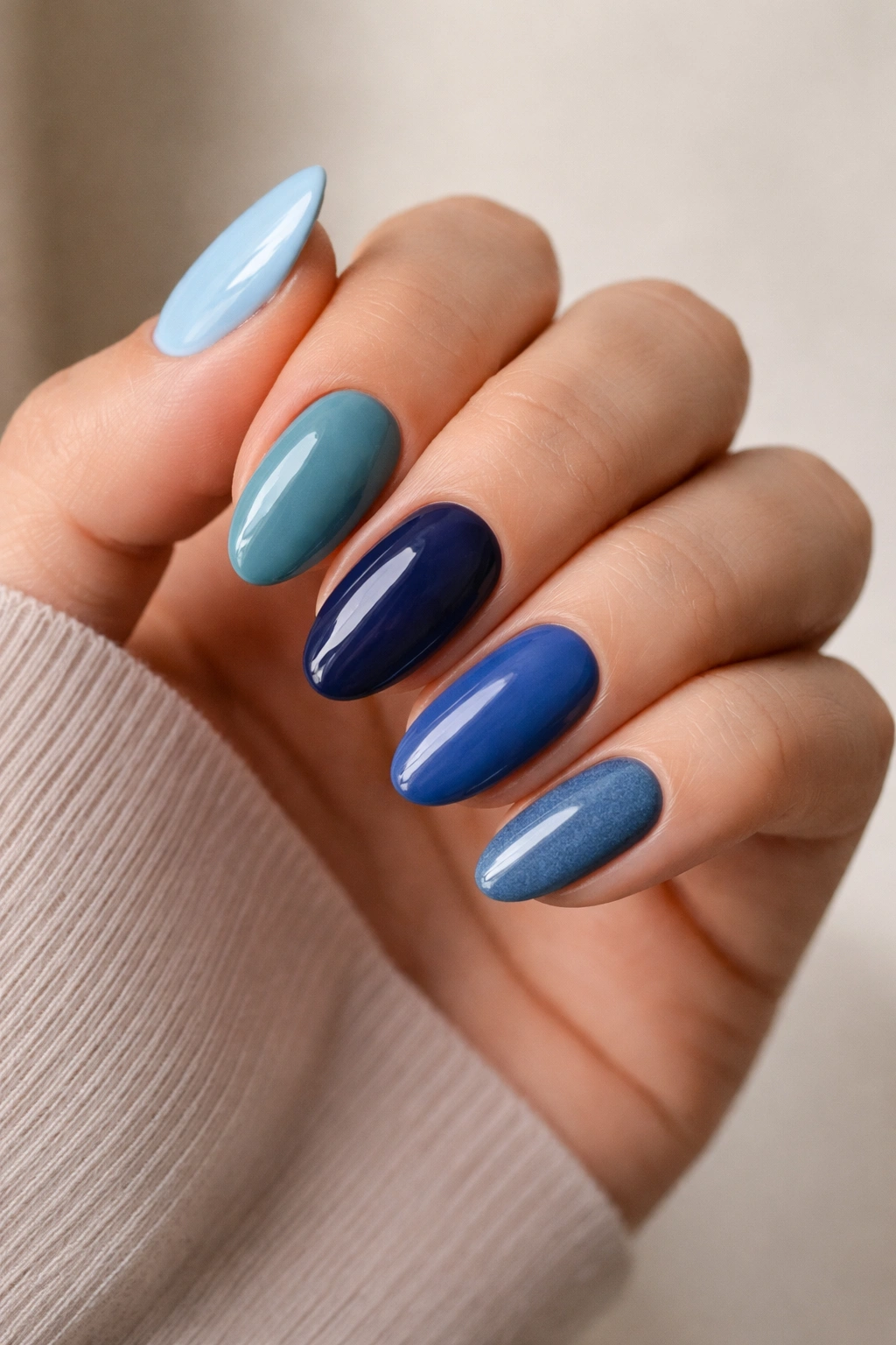 Close-up of five short blue almond nails in distinct blue shades