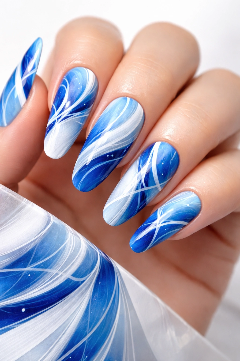 Close-up of blue and white abstract nail art on manicured nails against a plain background