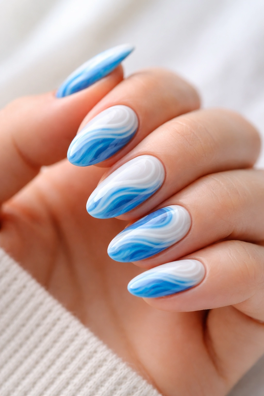 Close-up of short almond nails with blue and white ocean swirl nail art