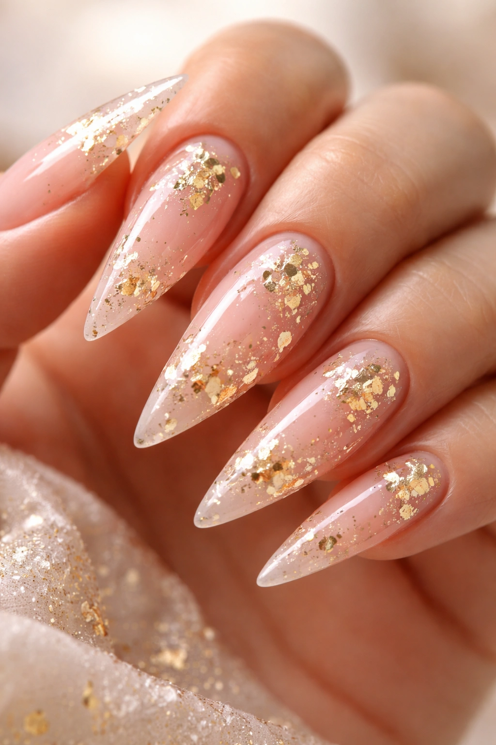 Soft blush pink nails with irregular gold leaf accents on stiletto tips