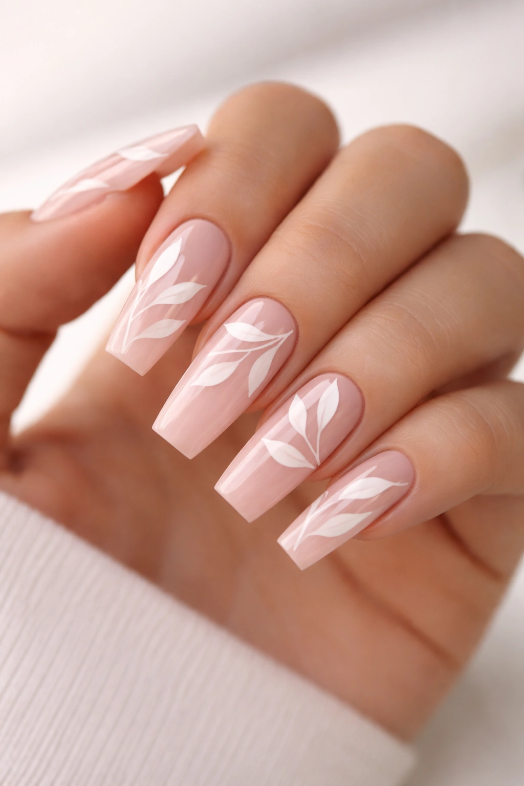 Close-up of soft blush coffin nails with white negative-space leaf design