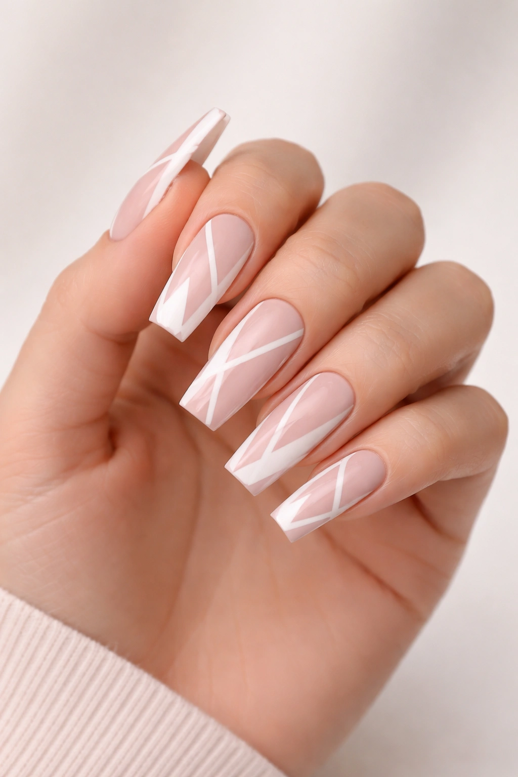Blush pink coffin nails with white geometric shapes on a bare hand