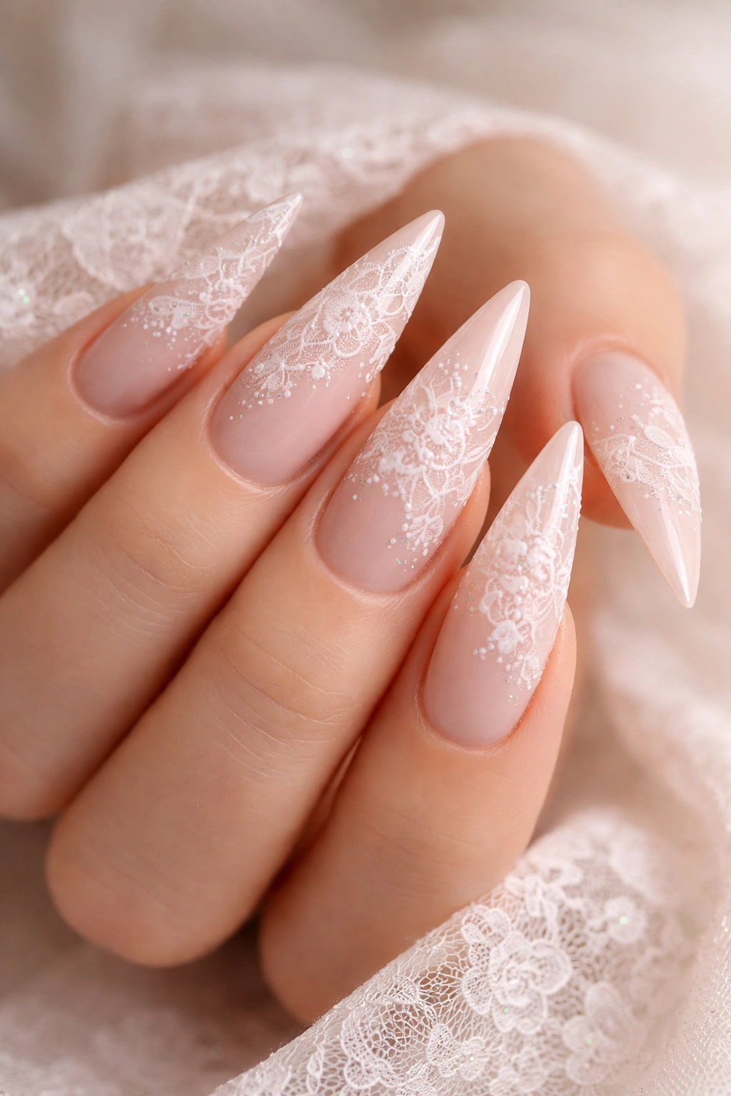 Close-up of blush pink nails with white lace pattern.