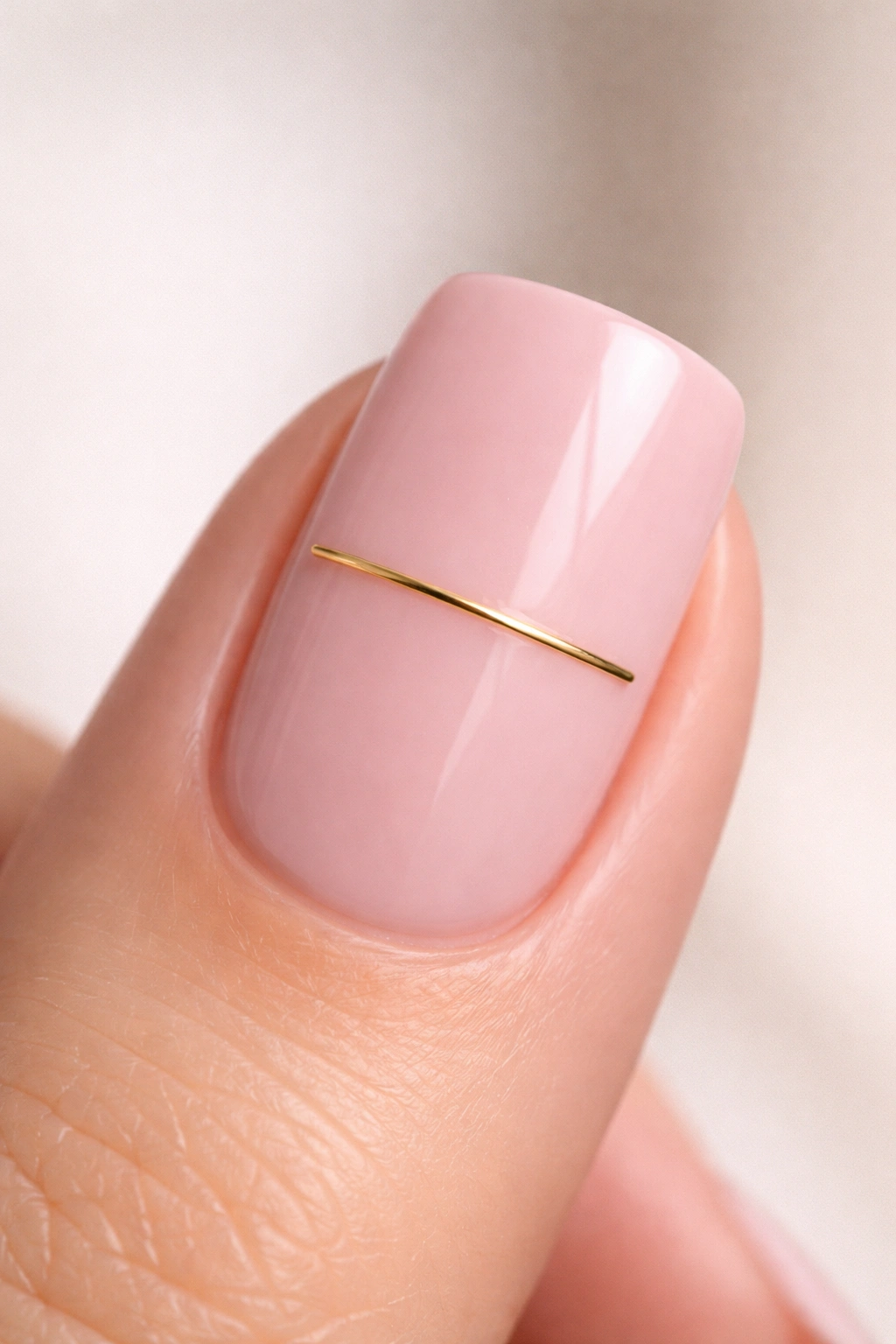 Close-up of blush pink nail with a slim gold bar charm across the center, minimalist design.
