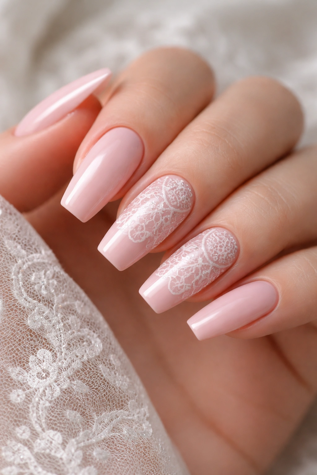 Close-up of blush pink coffin nails with delicate white lace design