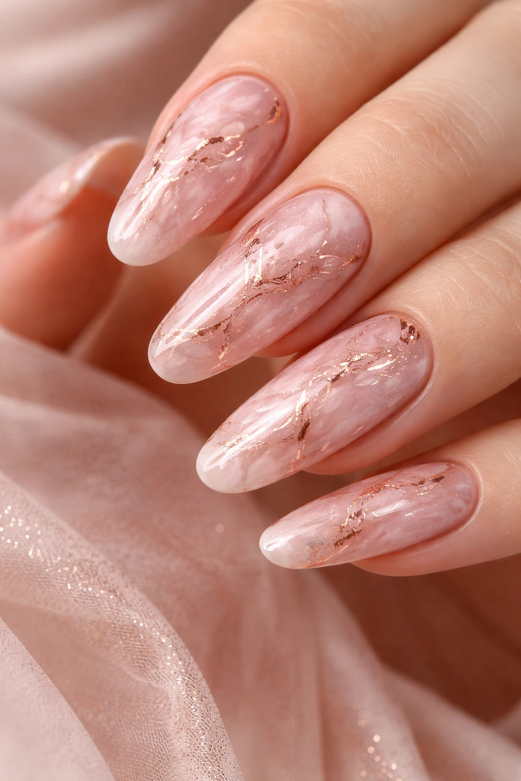 Close-up of long round nails with blush pink base and rose gold veining, glossy marble finish.