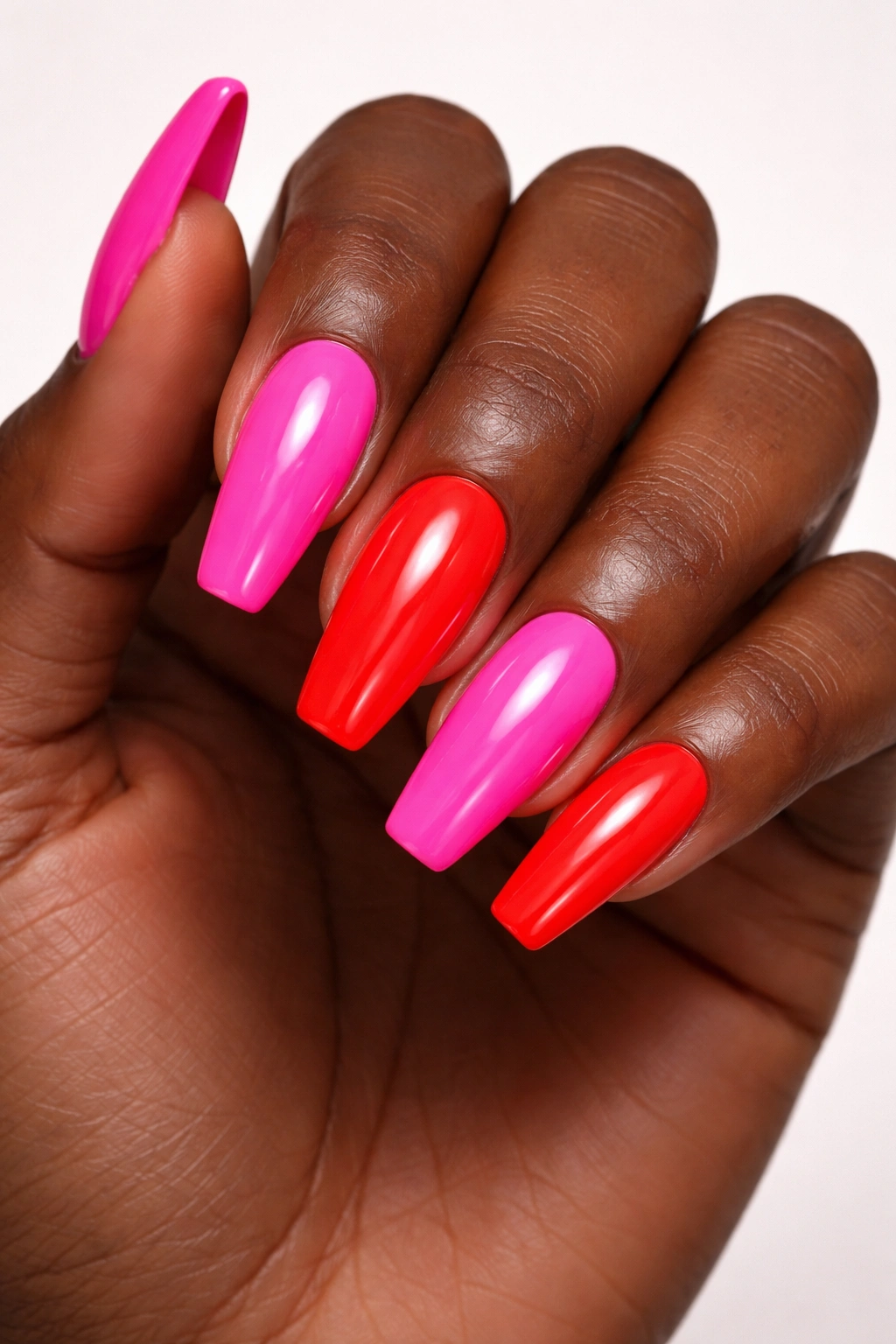Close-up of a hand with bold neon pink and red nails on dark skin.