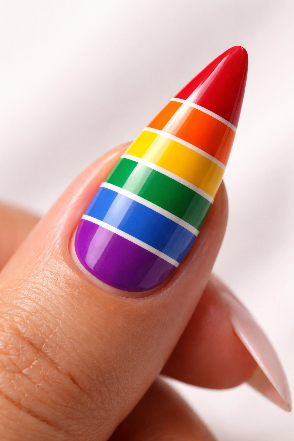Stiletto nail with bold rainbow stripes in six colors on a neutral background