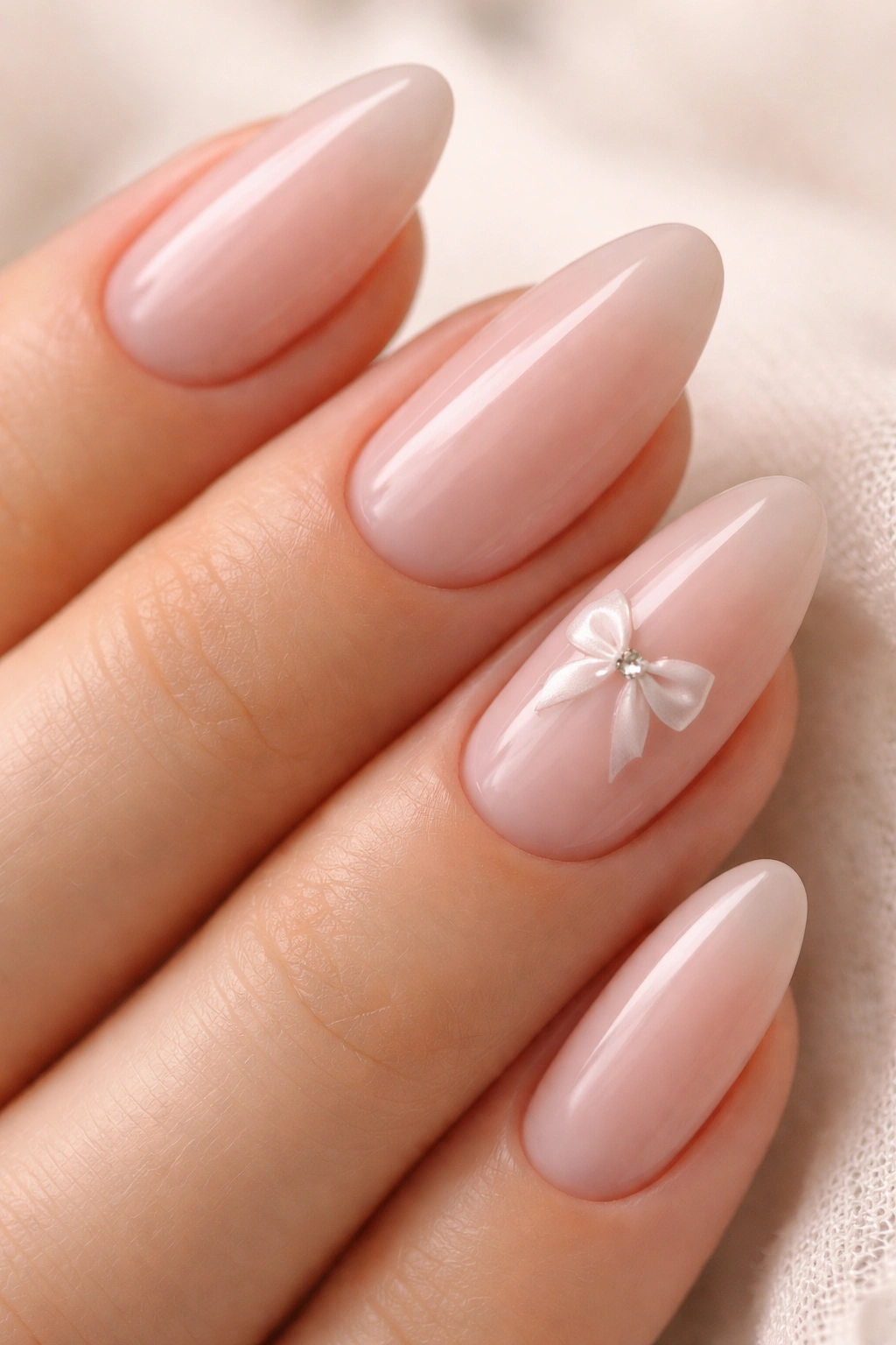 Almond nails featuring a tiny painted bow on one nail