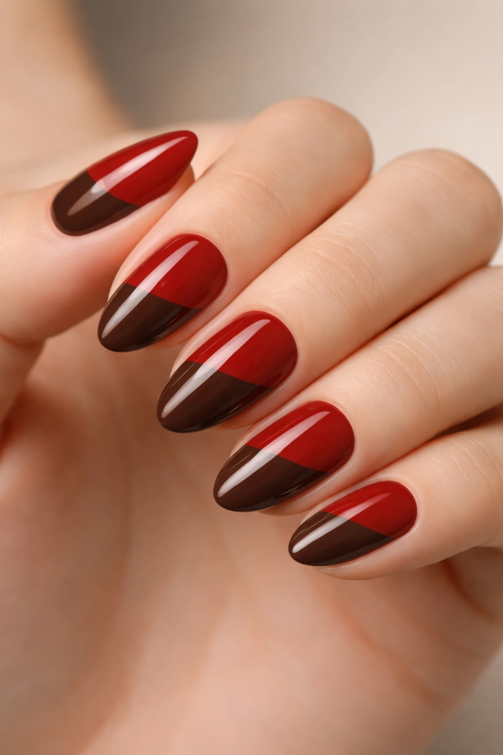 Close-up of short almond nails featuring brick red and chocolate brown color block with a sharp diagonal boundary