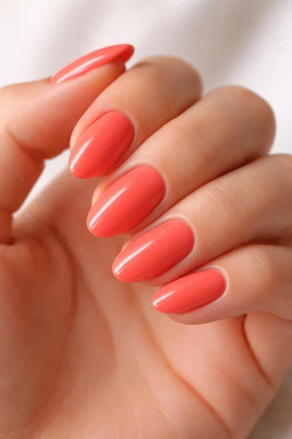 Close-up of short almond nails in bright coral polish