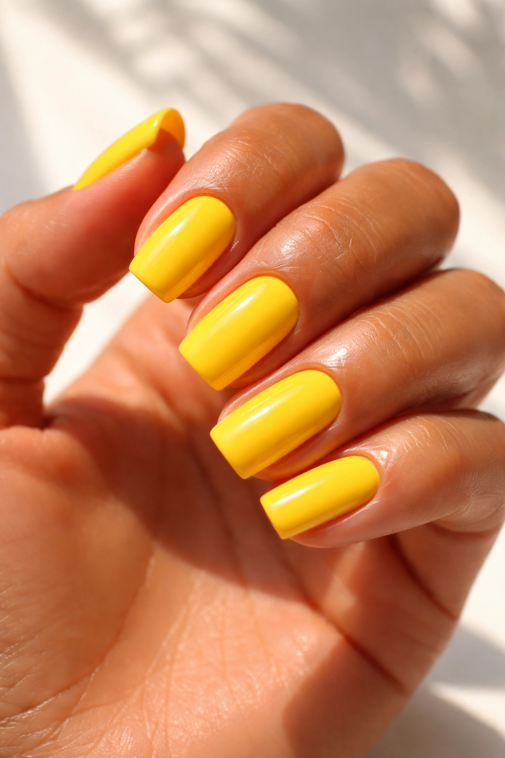 Close-up of bright yellow nails on tanned skin with glossy finish