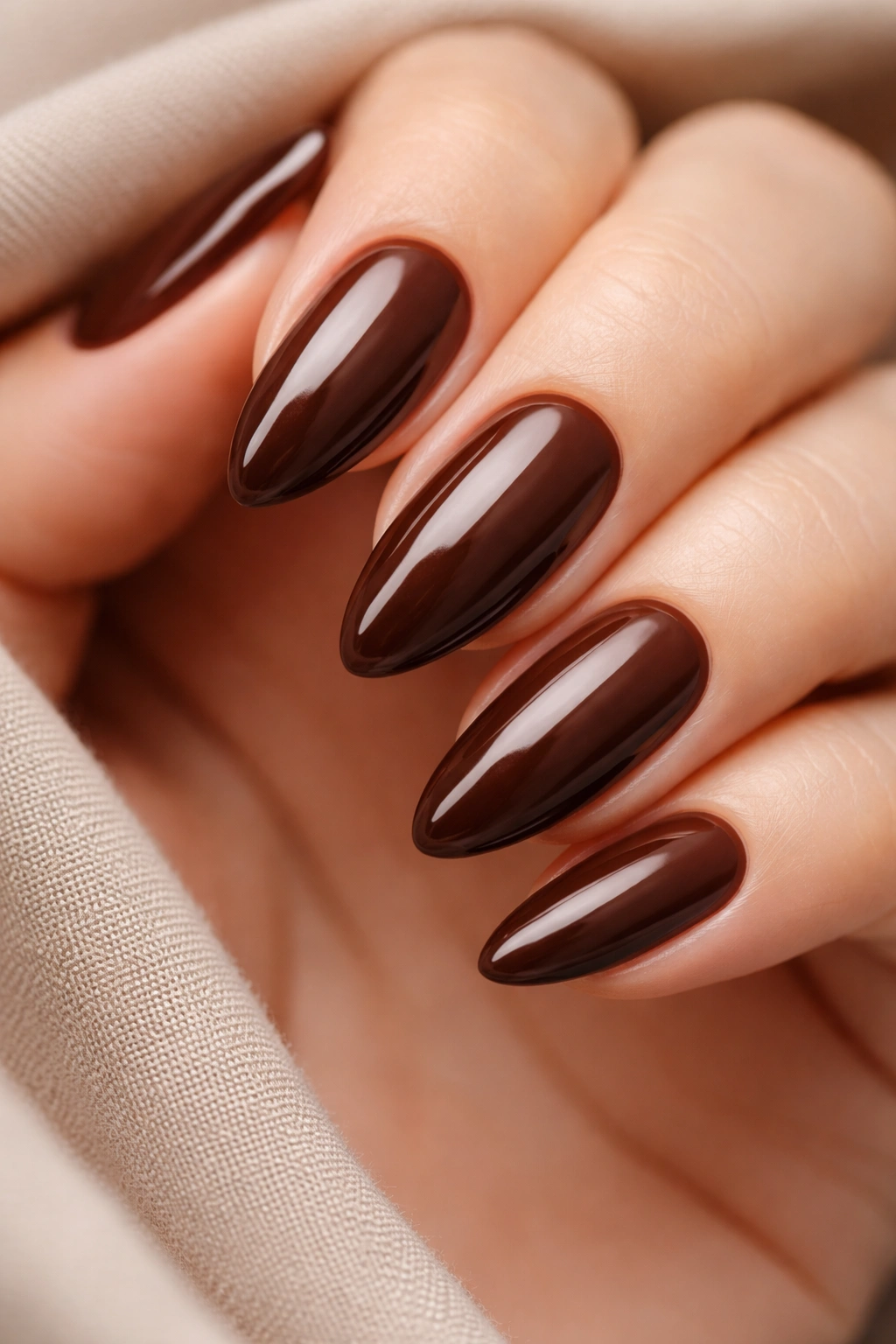 Close-up of brown almond nails with smooth coverage on neutral background