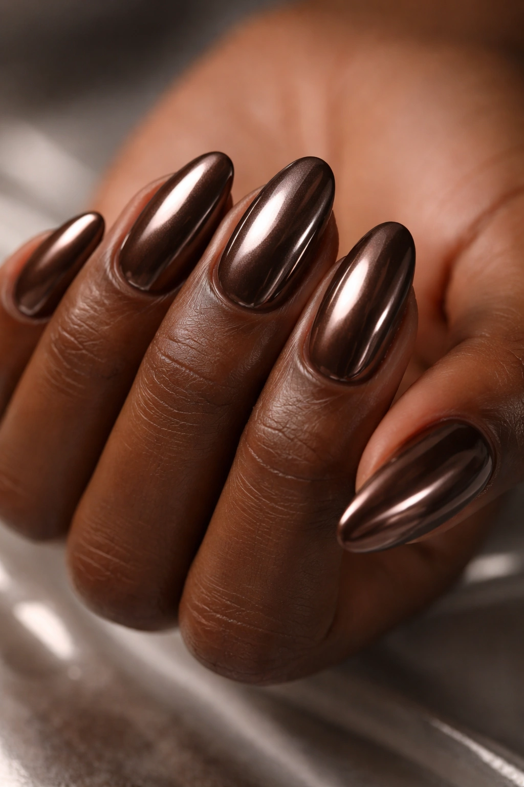 Close-up of short almond nails with brown chrome metallic finish on dark skin