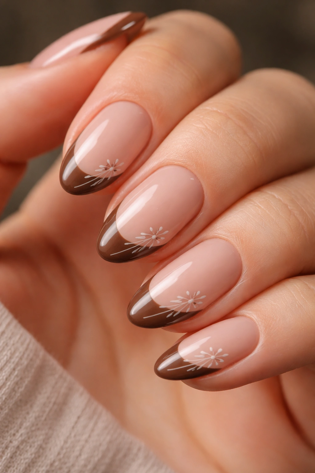 Close-up of short almond nails with brown tips and minimal floral line art at the tip.