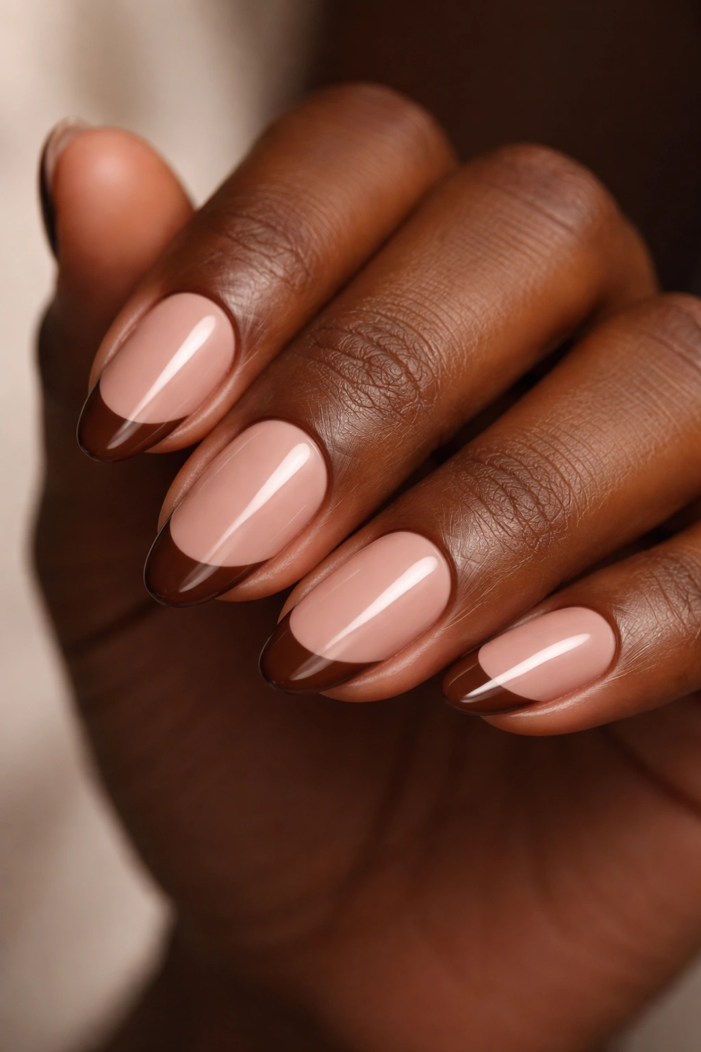 Close-up of short almond nails with nude base and brown tips on dark skin