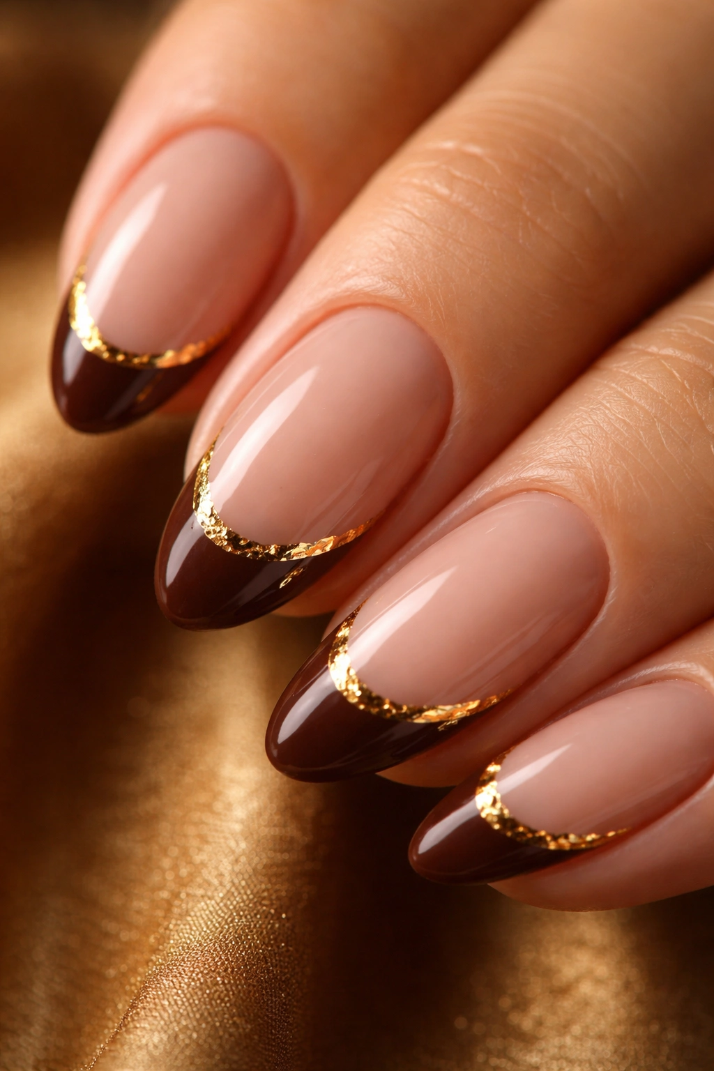 Close-up of a short almond nail with brown tip and thin gold foil edge