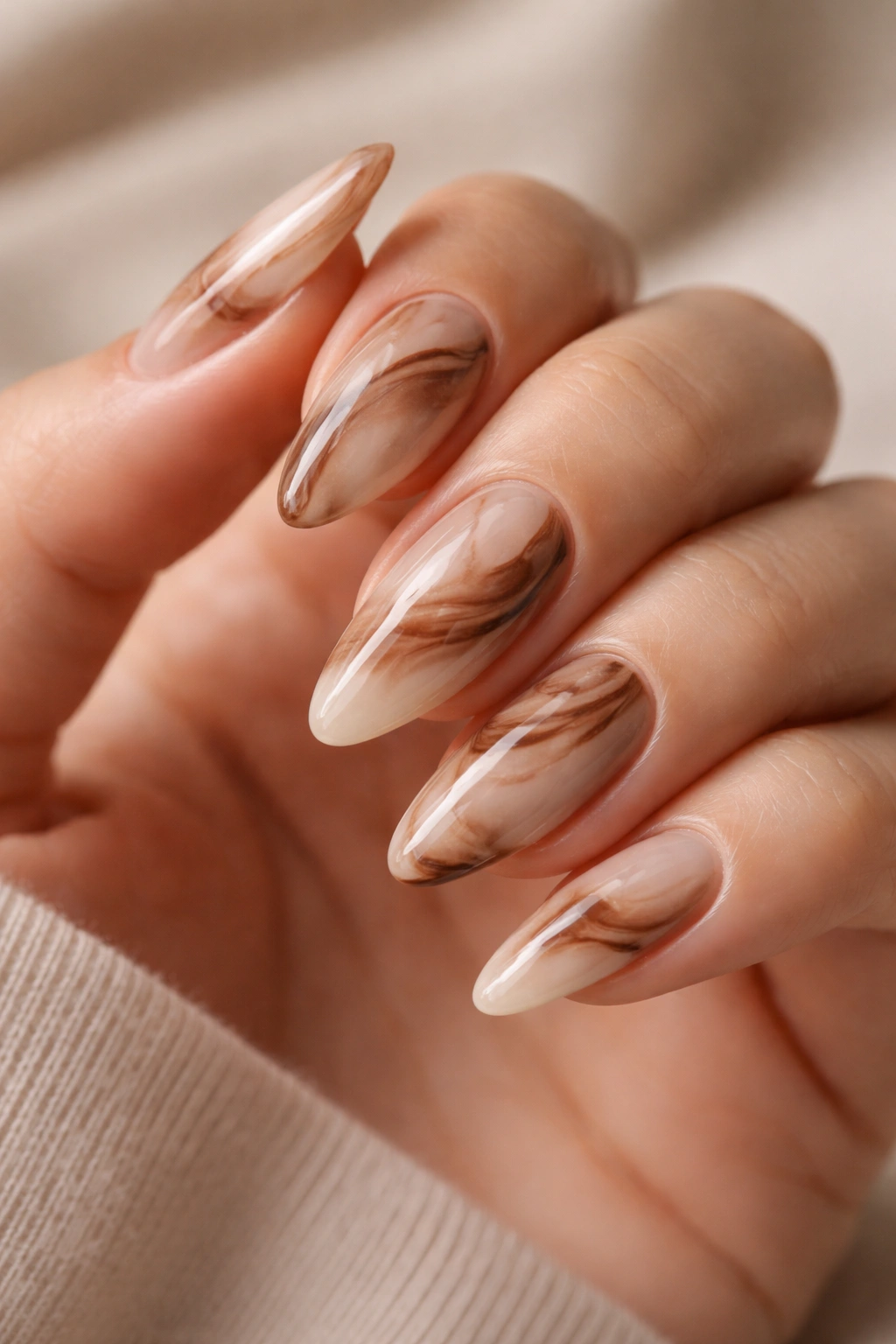 Close-up of brown marble almond nails with milky base on a neutral background