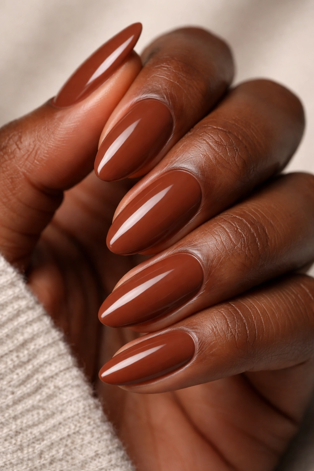 Close-up of a short almond nail painted warm cinnamon brown on dark skin.