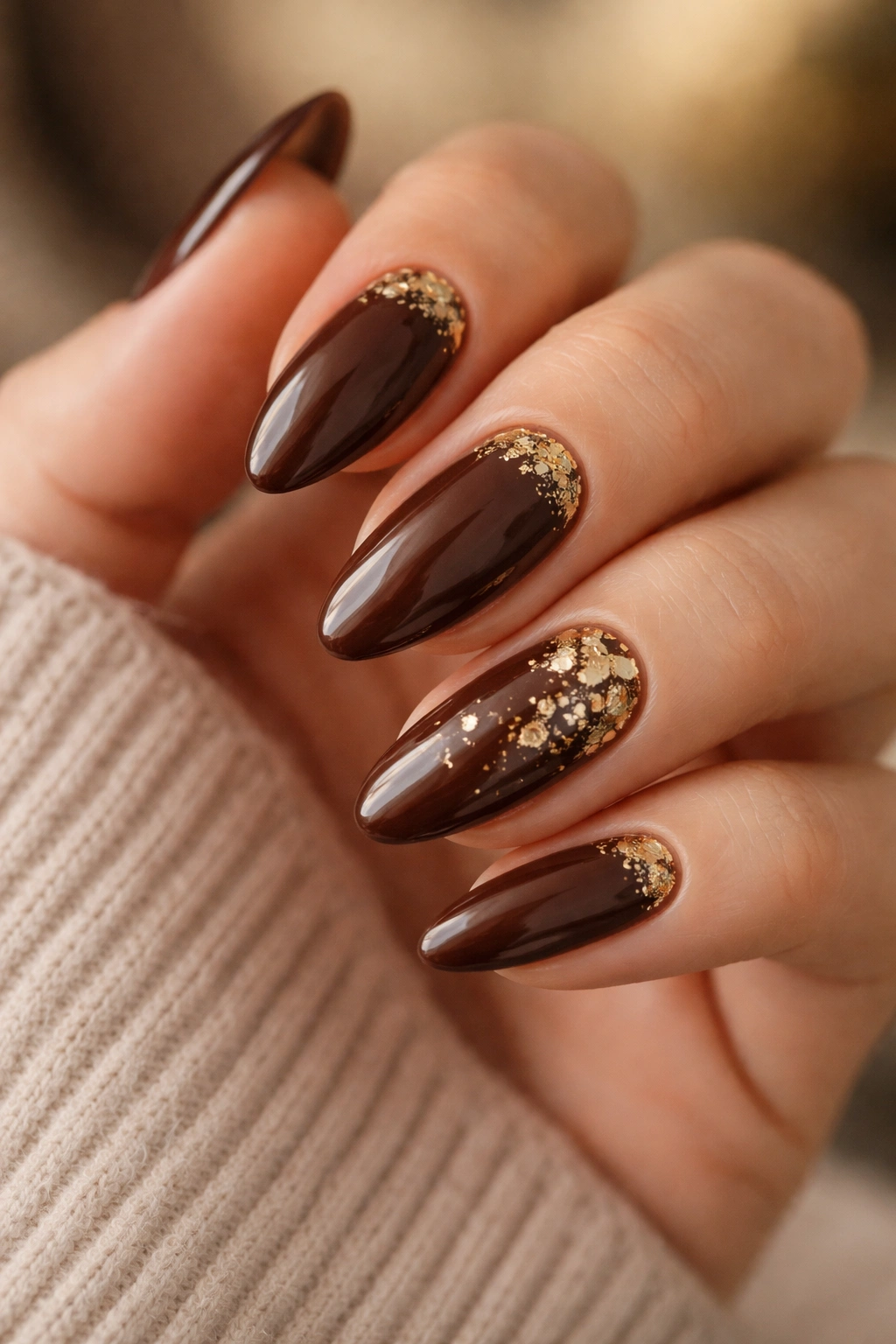 Brown almond nails with scattered gold foil accents on a clean background.
