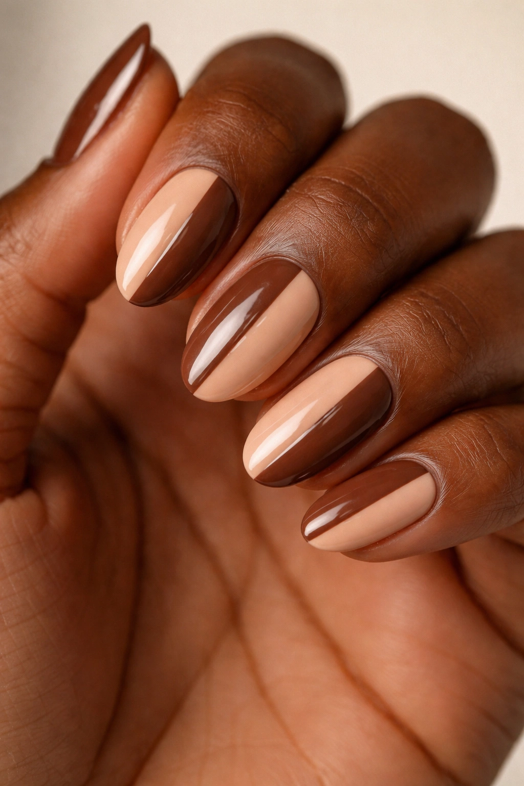 Close-up of a short almond nail with a brown and nude split design.