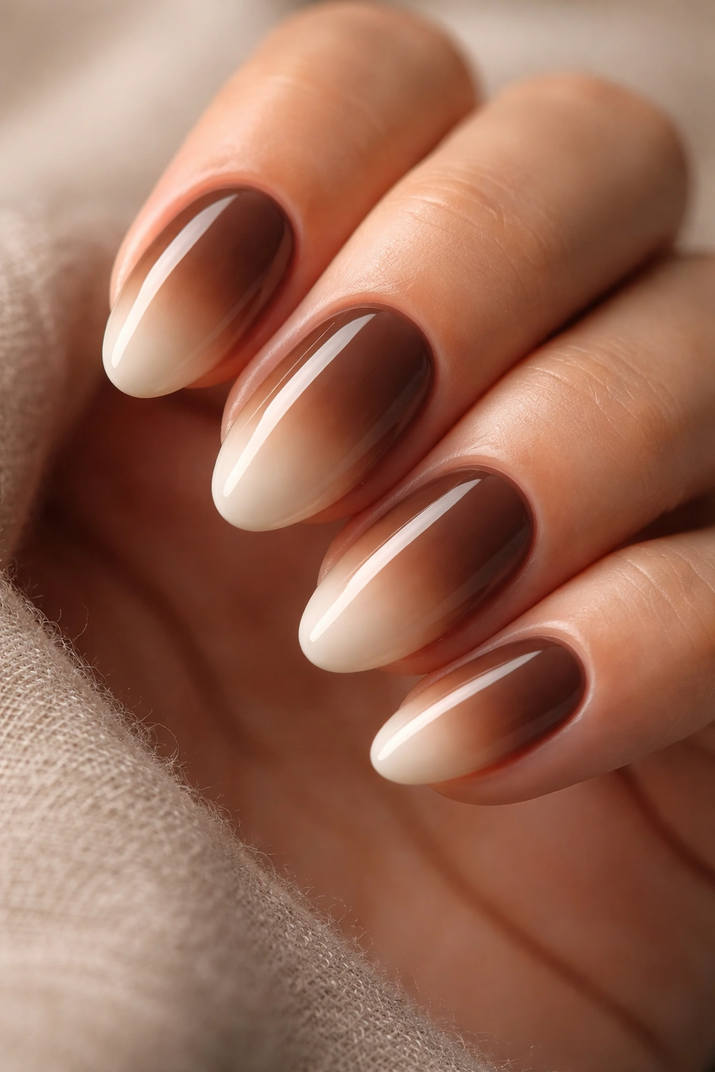 Close-up of short almond nails with brown to cream ombre and glossy finish