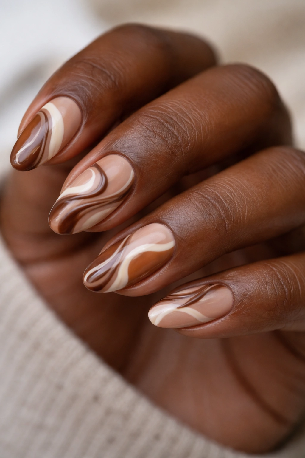 Close-up of brown swirl nail art on almond nails