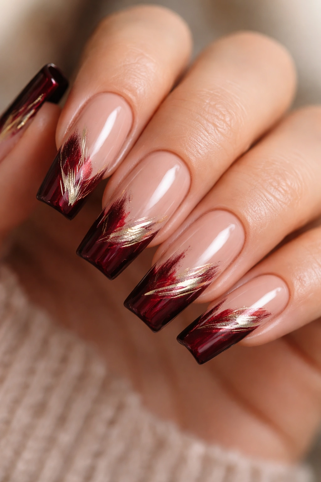 Nails with burgundy tips and gold brushstroke accents