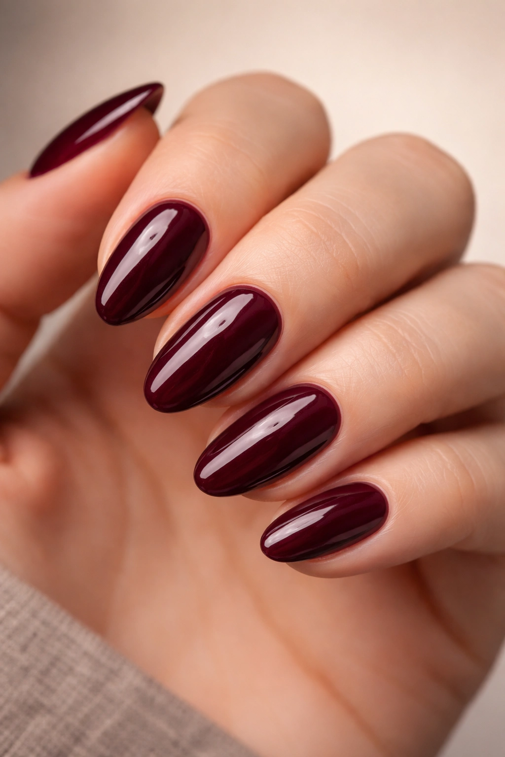 Close-up of deep burgundy almond nails on a hand with glossy finish