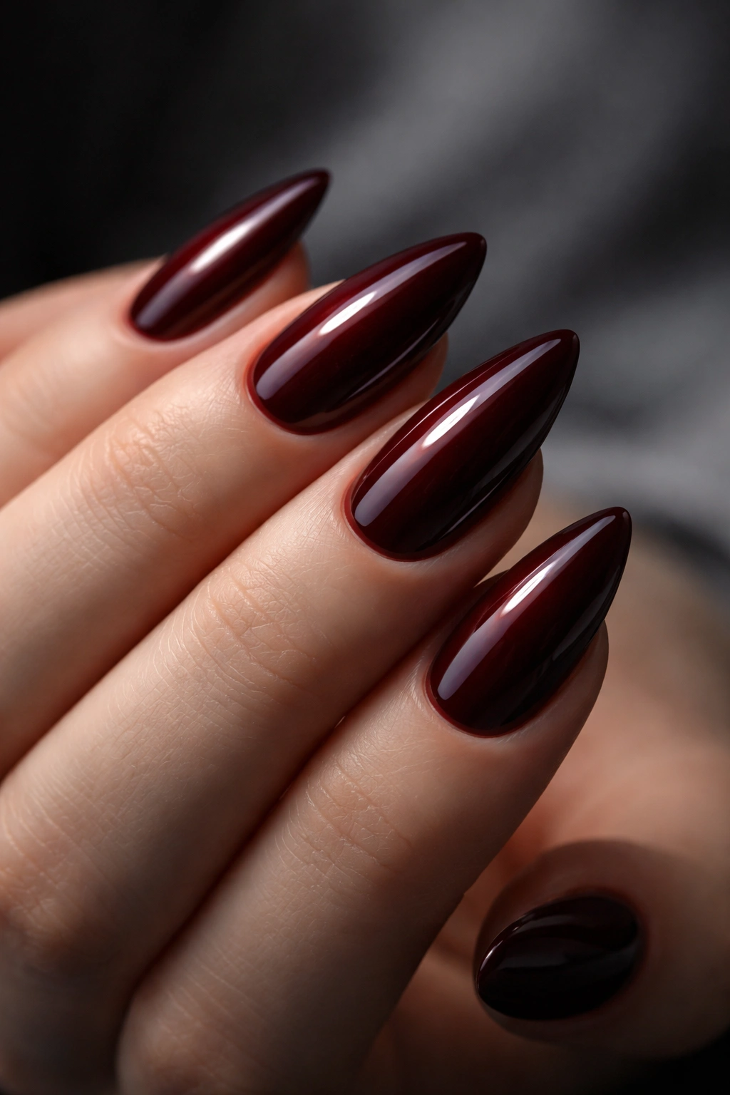 Close-up of deep burgundy almond nails under cool lighting