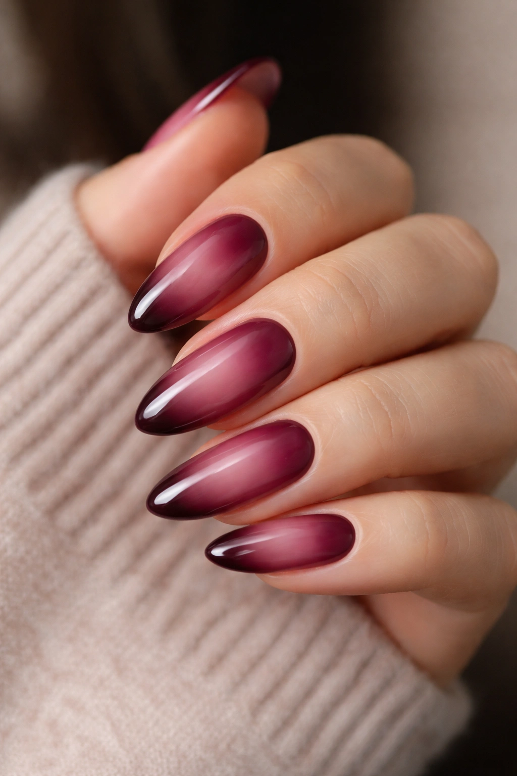Close-up of burgundy aura nails showing a soft center glow with darker edge on long oval nails