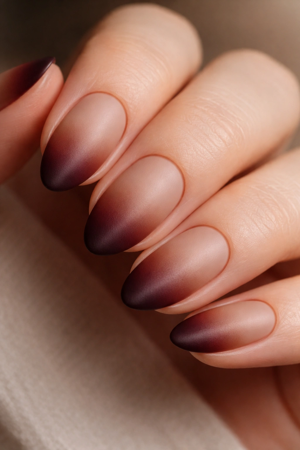 Close-up of a short almond nail with brown tip blending into burgundy