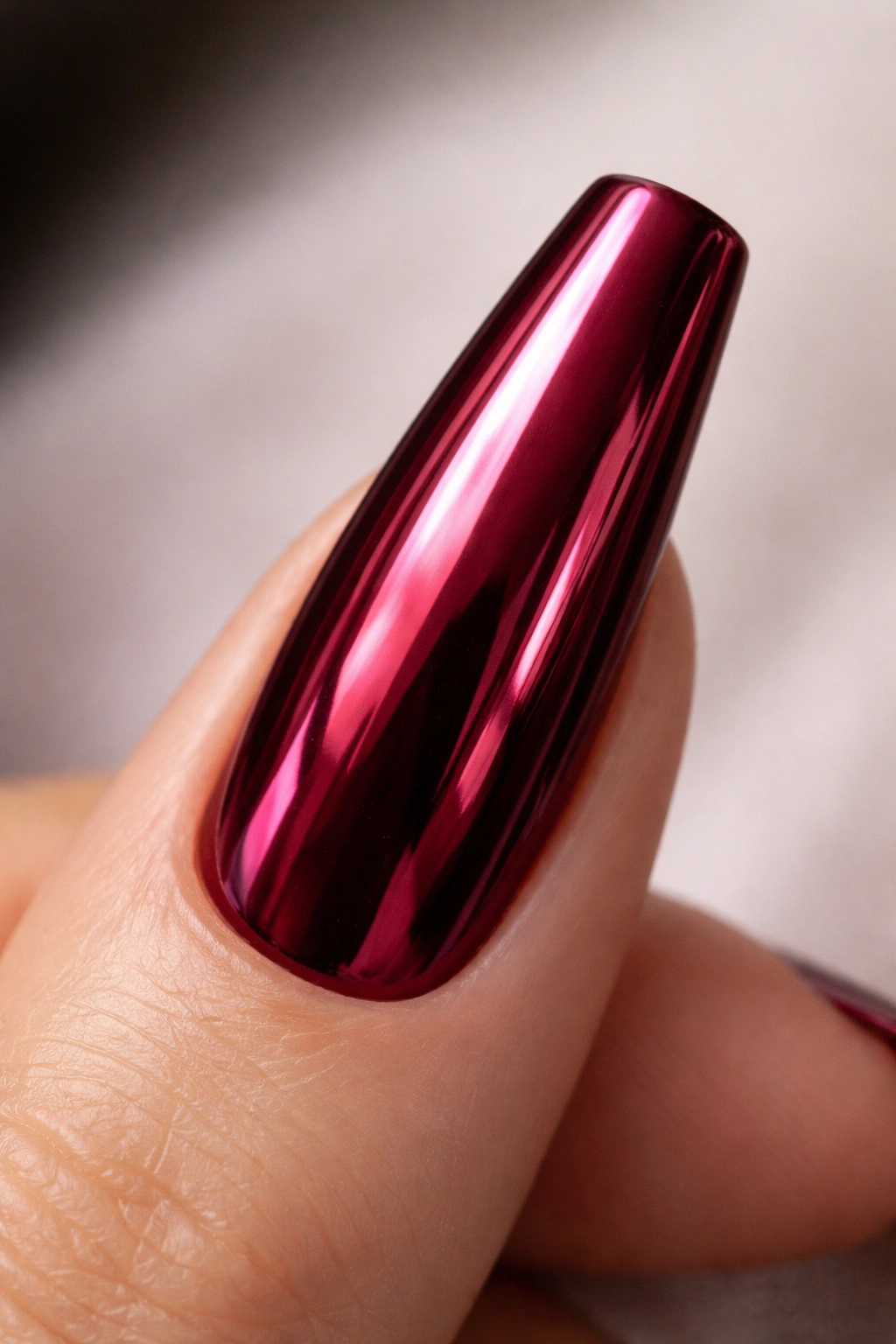 Close-up of a long coffin nail with a deep burgundy chrome mirror finish