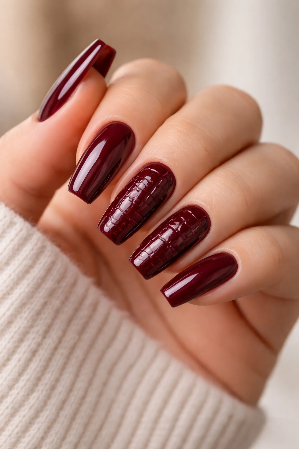 Close-up of burgundy croc-textured nails on a hand with plain glossy nails