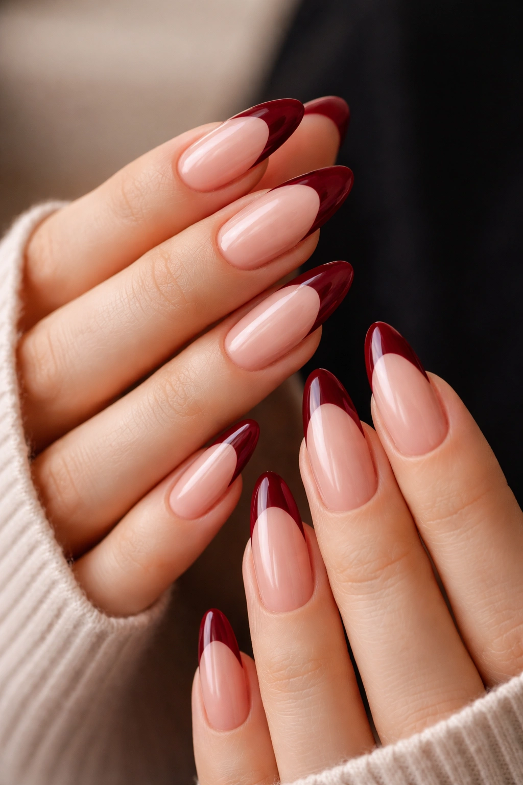 Close-up of burgundy French tips on long oval nails with sheer pink base.