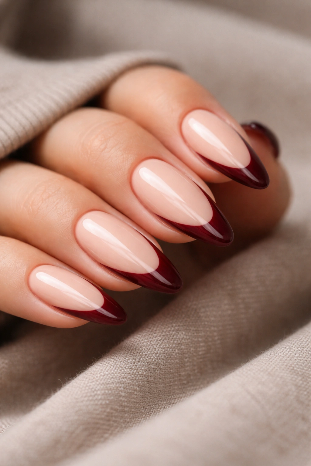 Close-up of almond nails with burgundy tips on beige nude base