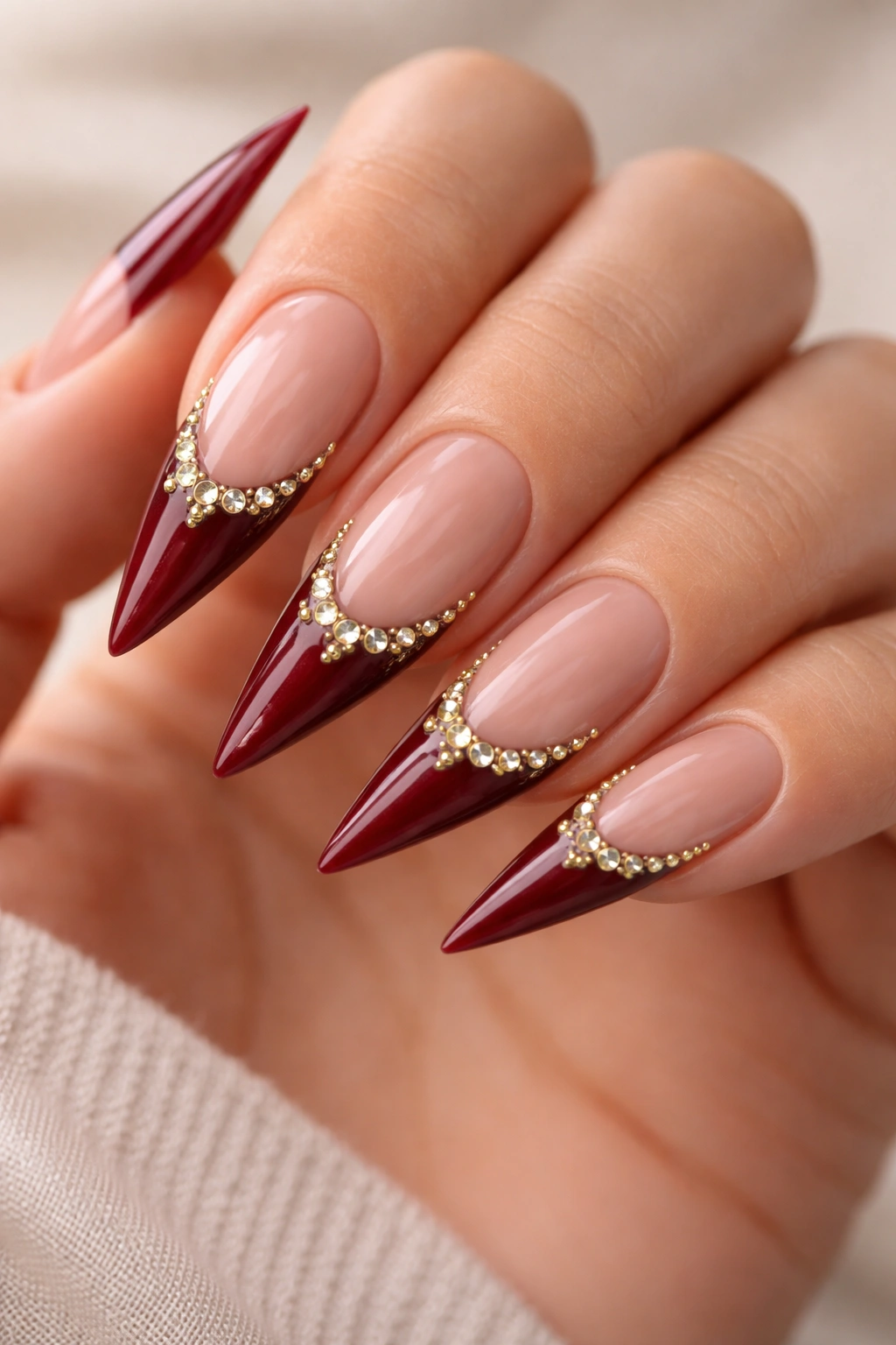 Stiletto nails with burgundy tips and gold rhinestones along smile line
