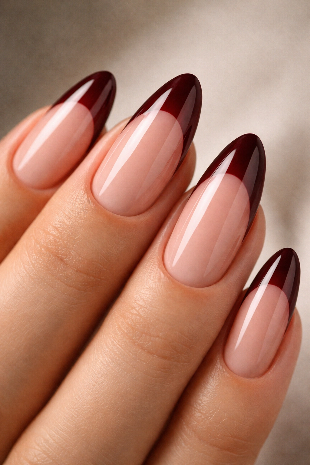 Close-up of almond nails with burgundy tips and high-gloss finish