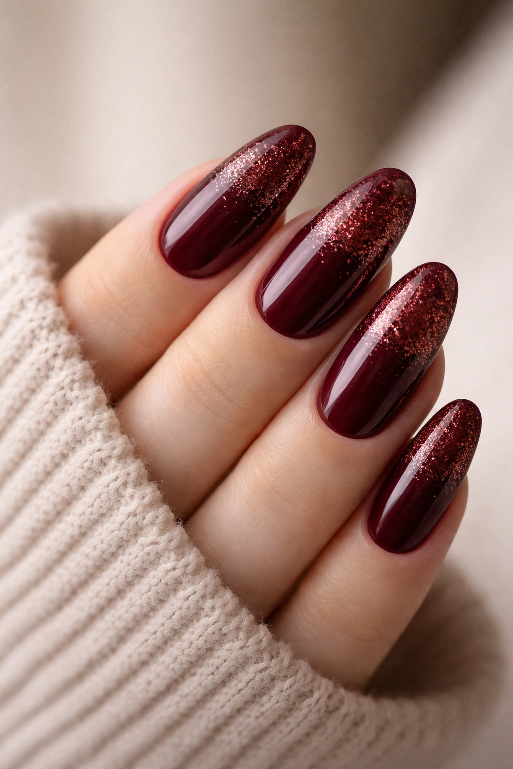 Close-up of burgundy long oval nails with a glitter gradient fading toward the tips