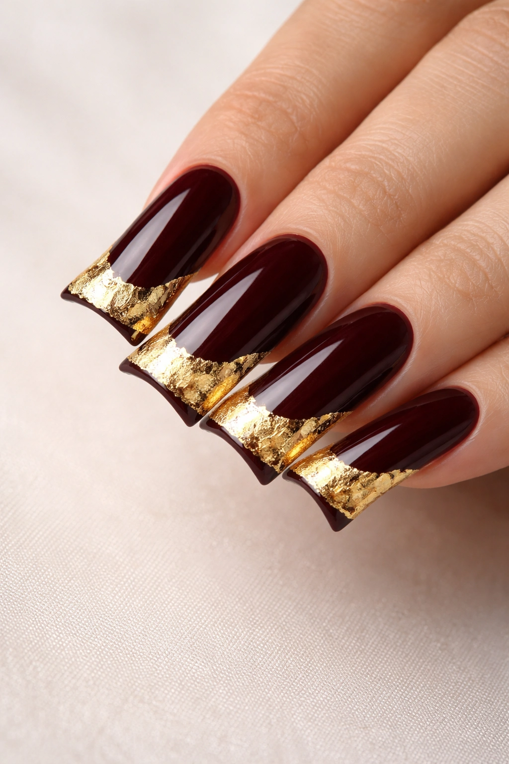 Long duck nails with burgundy base and gold foil tip in glossy finish.