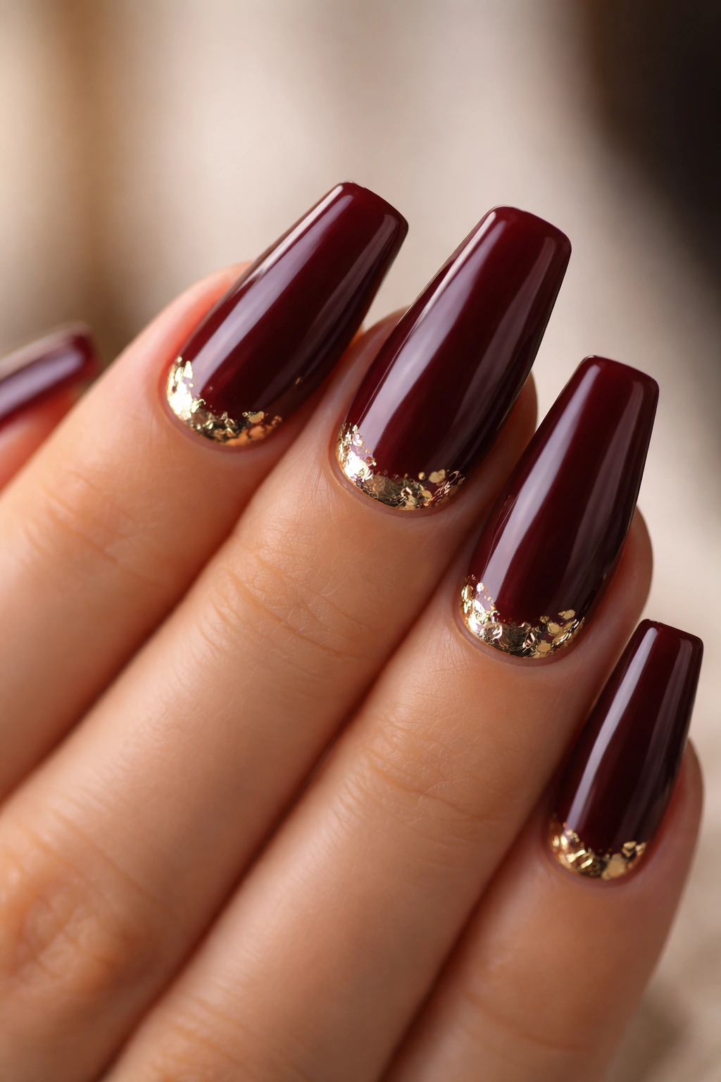 Close-up burgundy nails with delicate gold foil near the cuticle