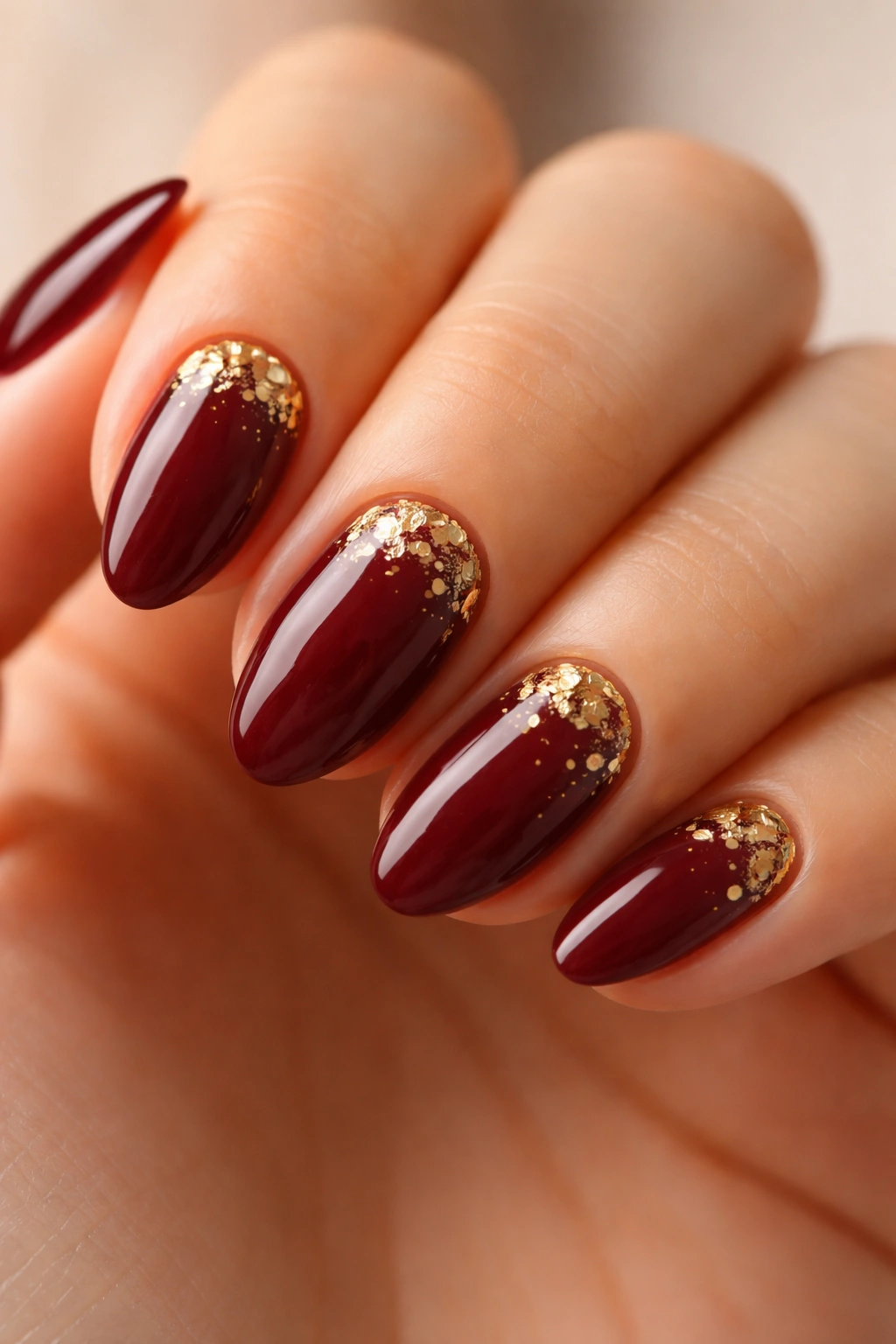 Short almond nails with burgundy base and gold foil accents close-up