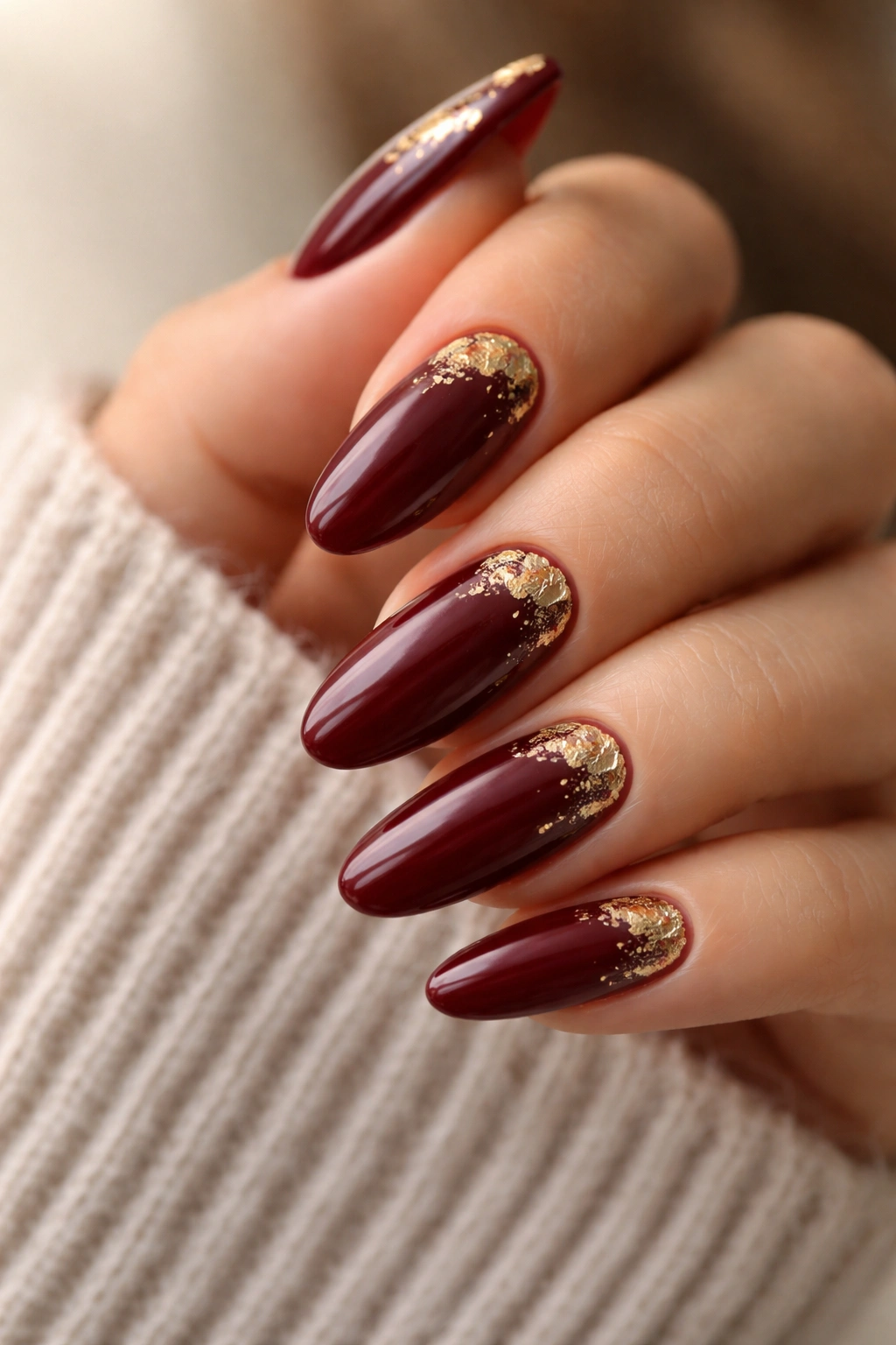 Close-up of burgundy nails with gold foil accents on long oval nails.