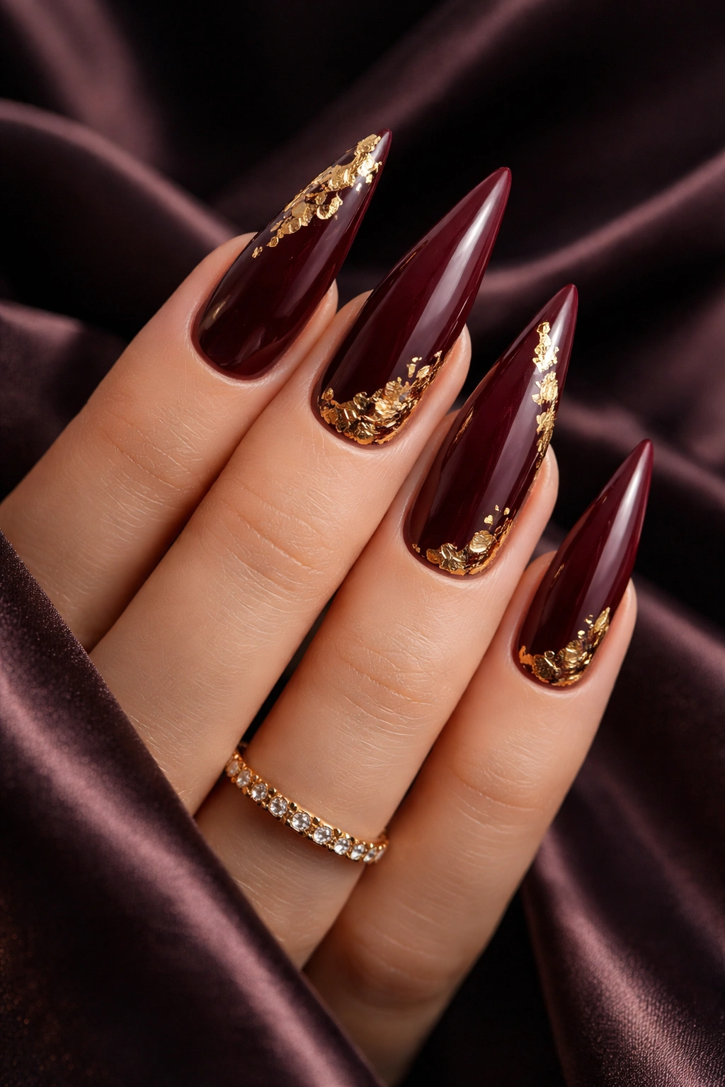 Deep burgundy nails with gold leaf accents catching light