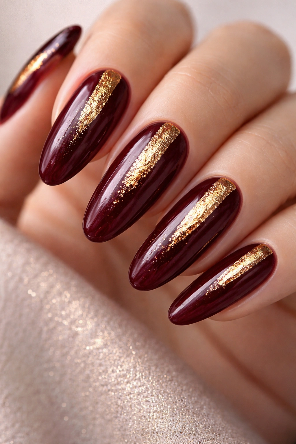 Close-up of deep burgundy long-oval nails with gold foil accents