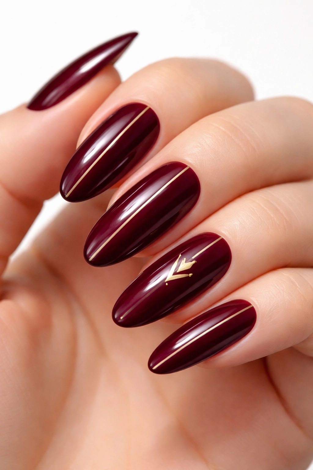 Long oval burgundy nails with gold geometric lines, metallic shine