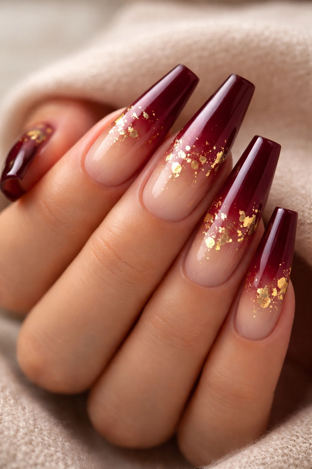 Close-up of coffin nails with burgundy to nude gradient and gold leaf accents