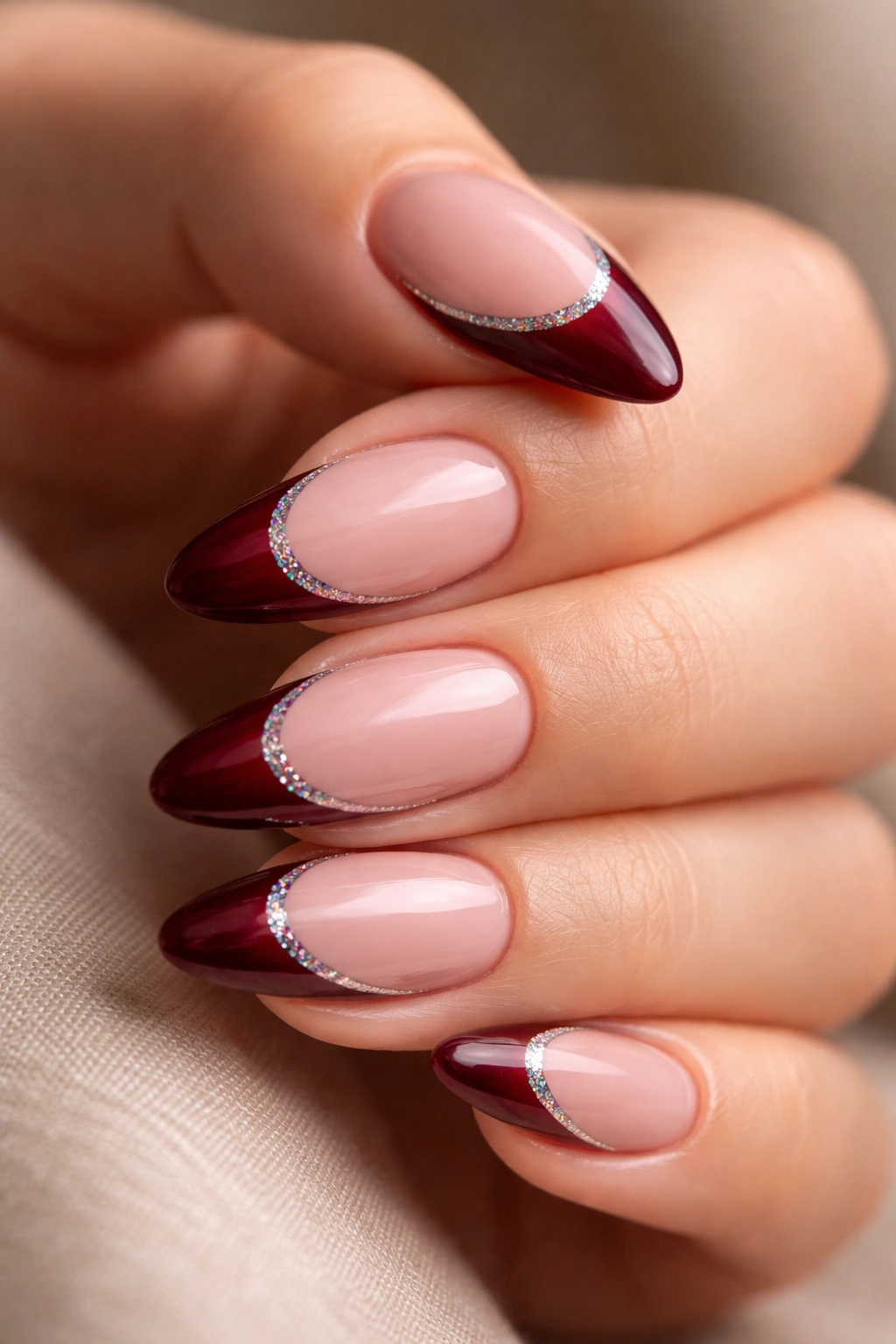 Close-up of almond nails with burgundy tips and holographic glitter crescent