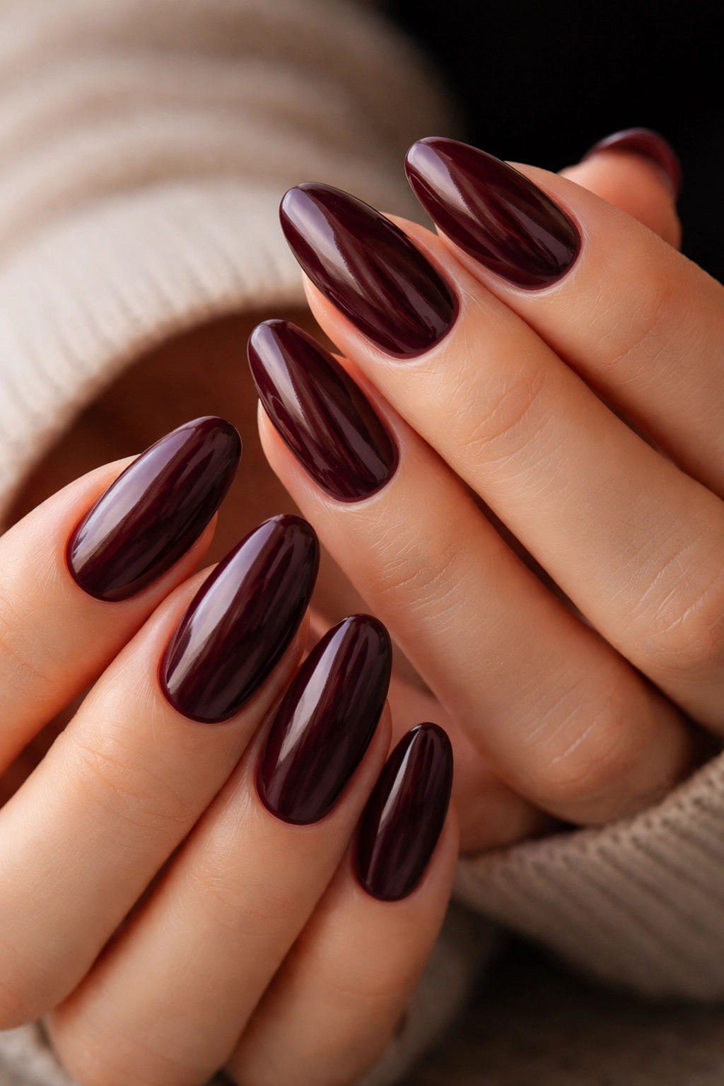Close-up of deep burgundy long oval nails with a glassy high-gloss finish showing color shifts.