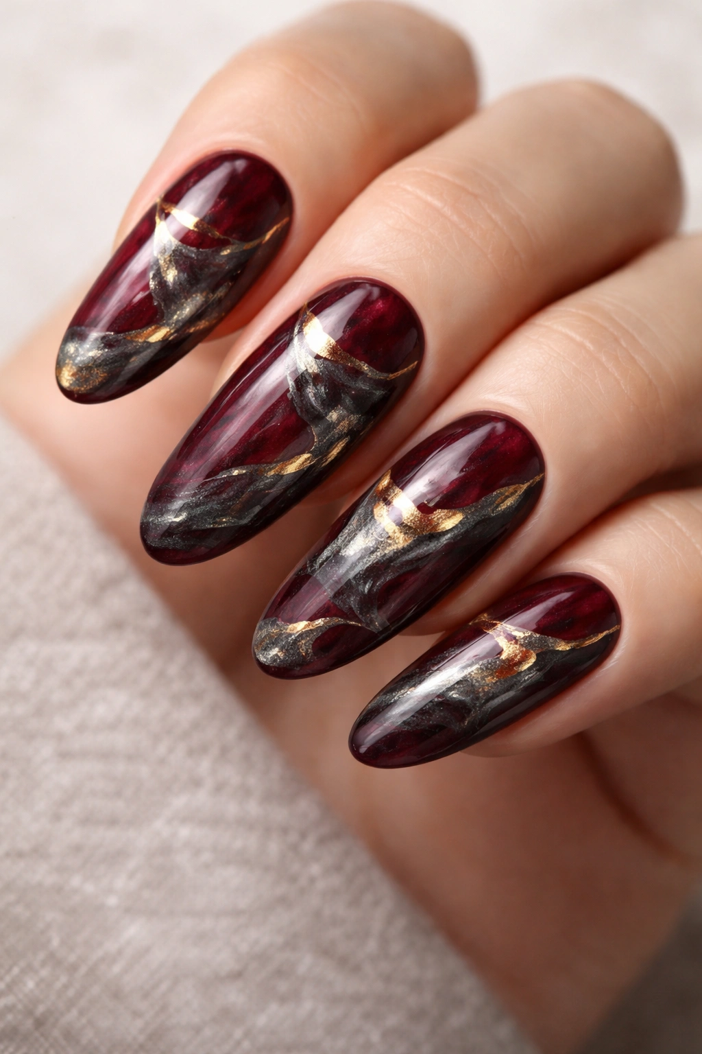 Close-up of long oval burgundy nails with charcoal and gold marble swirls
